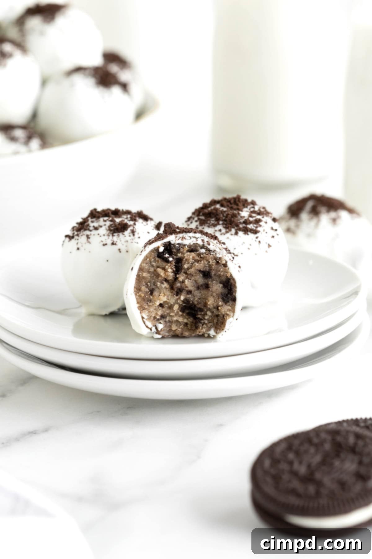 There Oreo cake balls on a stack of three white plates. The front cake ball has a bite out of it.