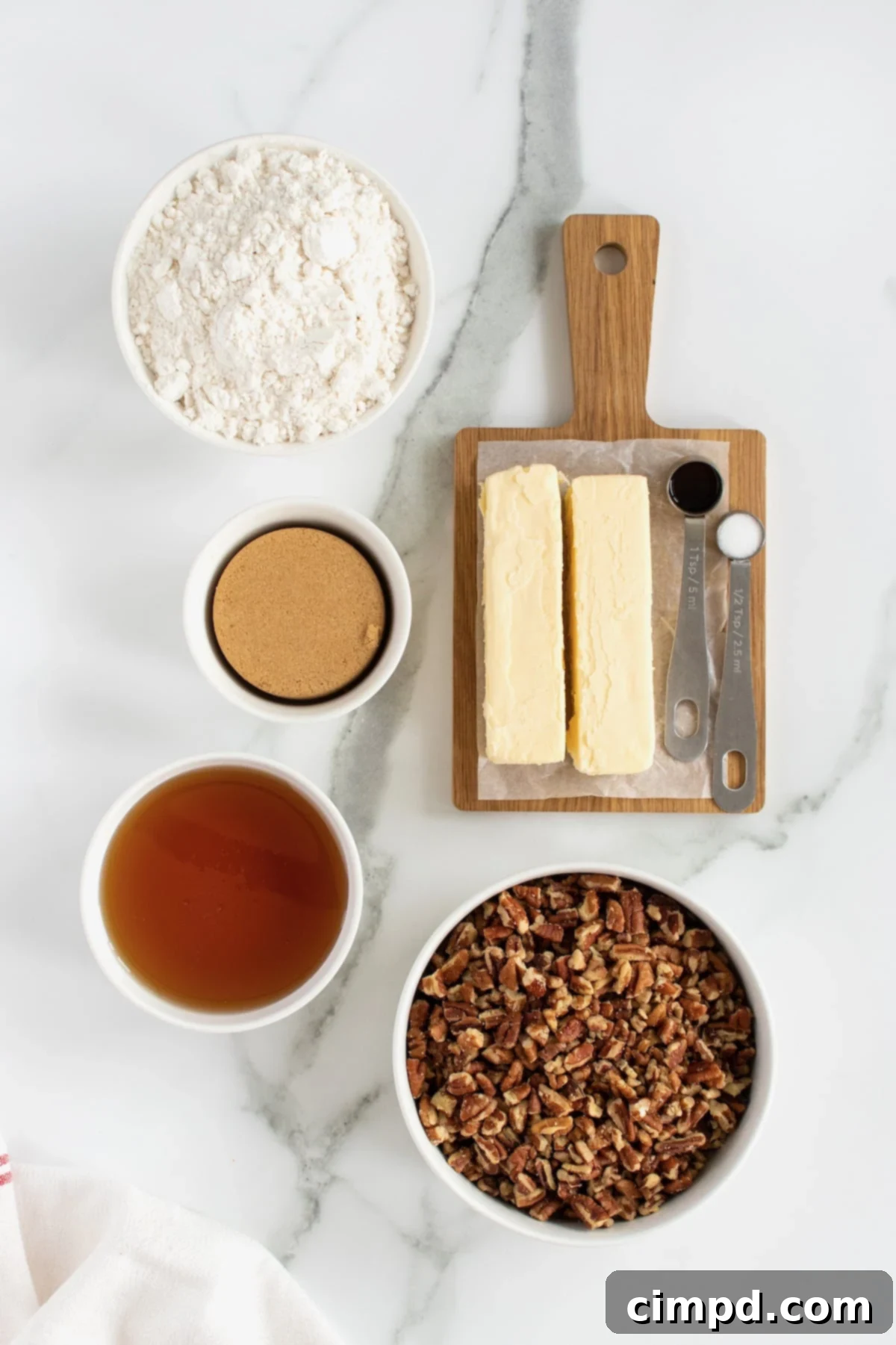 A collection of fresh ingredients for Pecan Pie Bites, including a bowl of chopped pecans, sticks of butter, brown sugar, and a bottle of corn syrup.