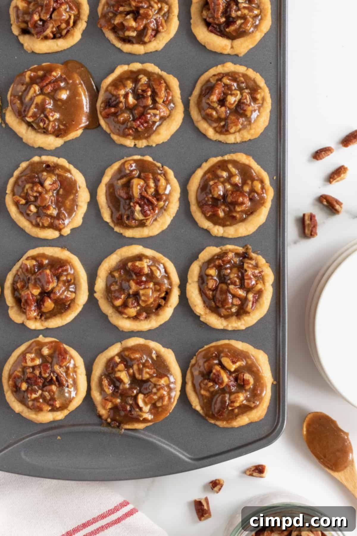 Freshly baked Pecan Pie Bites cooling in the muffin tin, with the second layer of filling added, showcasing their gooey tops.