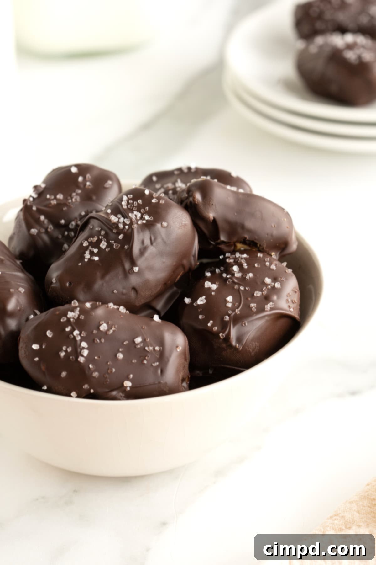 Salted Dark Chocolate Peanut Butter Stuffed Dates 4 A white serving bowl filled with chocolate covered dates sprinkled with sea salt.