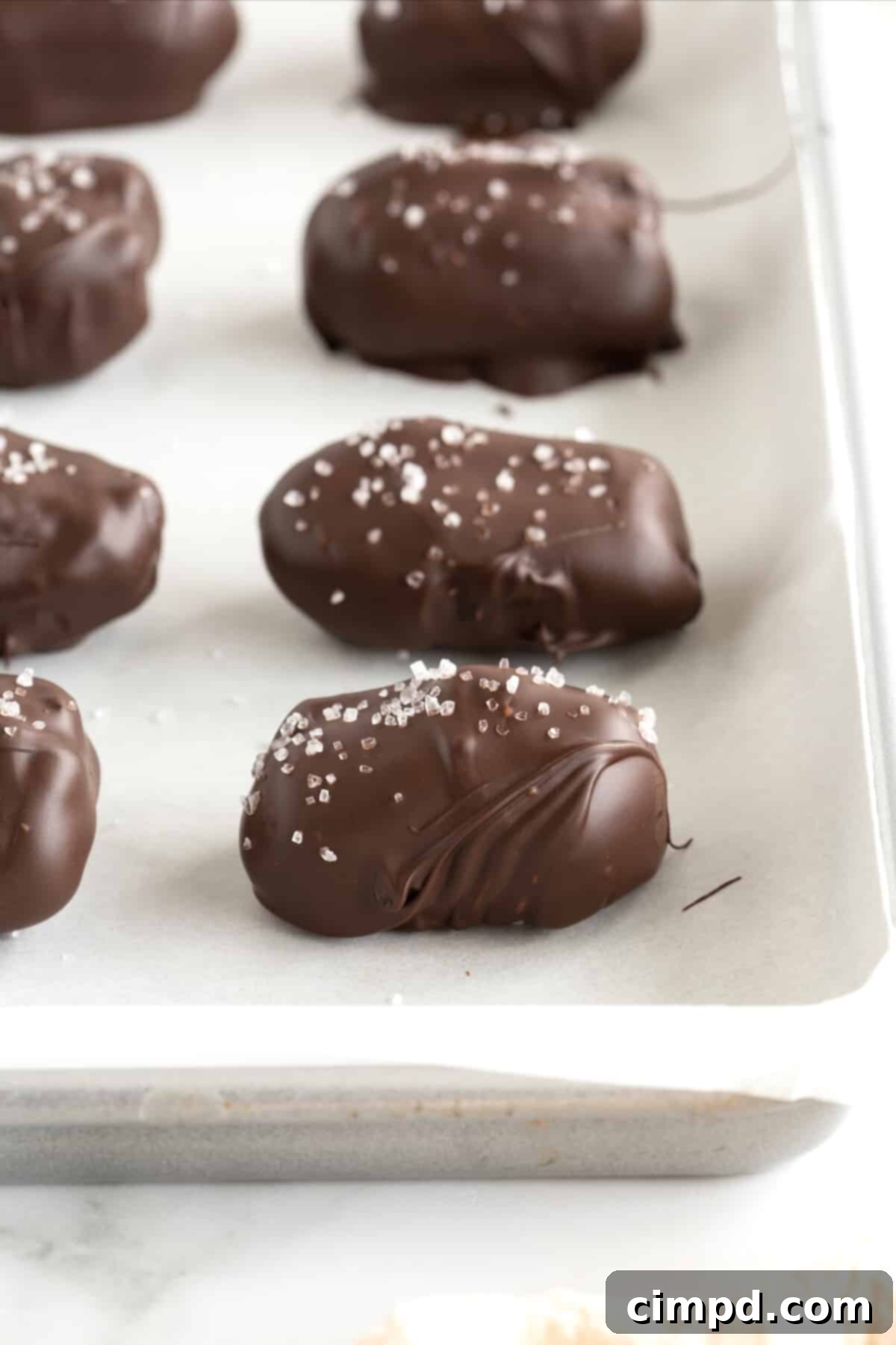Salted Dark Chocolate Peanut Butter Stuffed Dates 9 Chocolate covered dates sprinkled with sea salt on a parchment lined baking sheet.