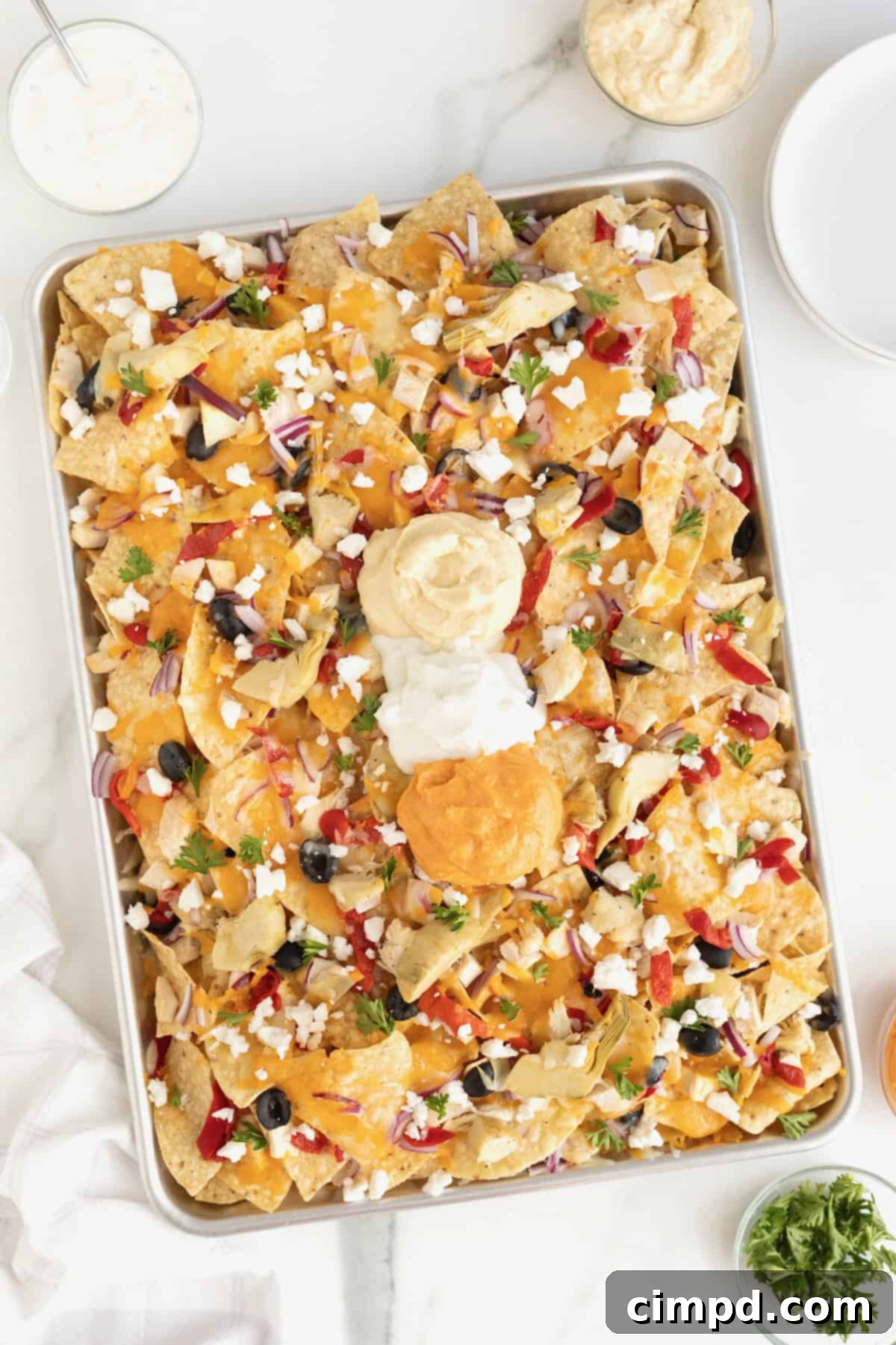 A sheet pan full of Mediterranean nachos on a white marble counter, garnished with fresh herbs.