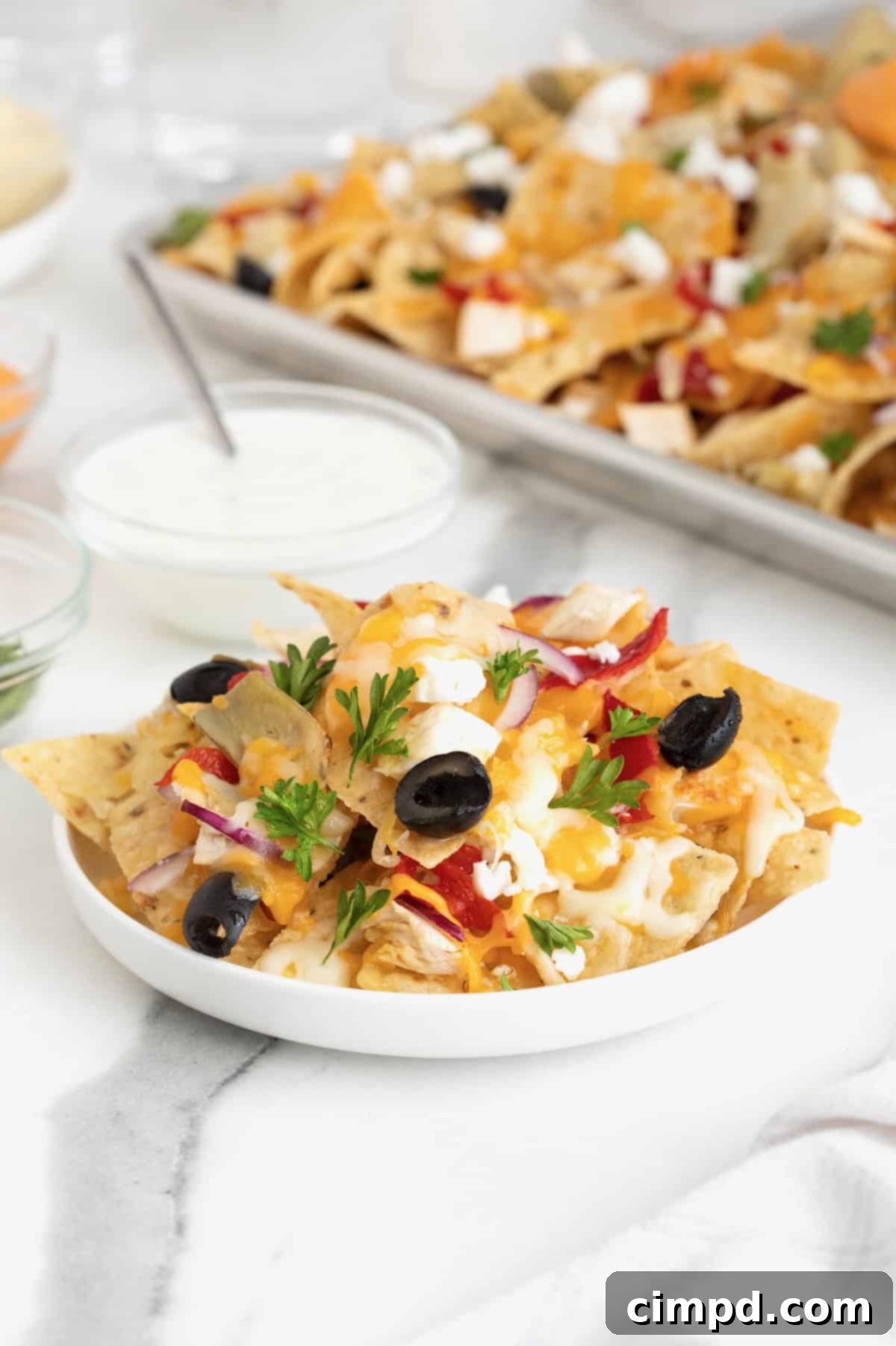 A serving of Mediterranean nachos on a white plate, with a side bowl of sour cream or tzatziki.