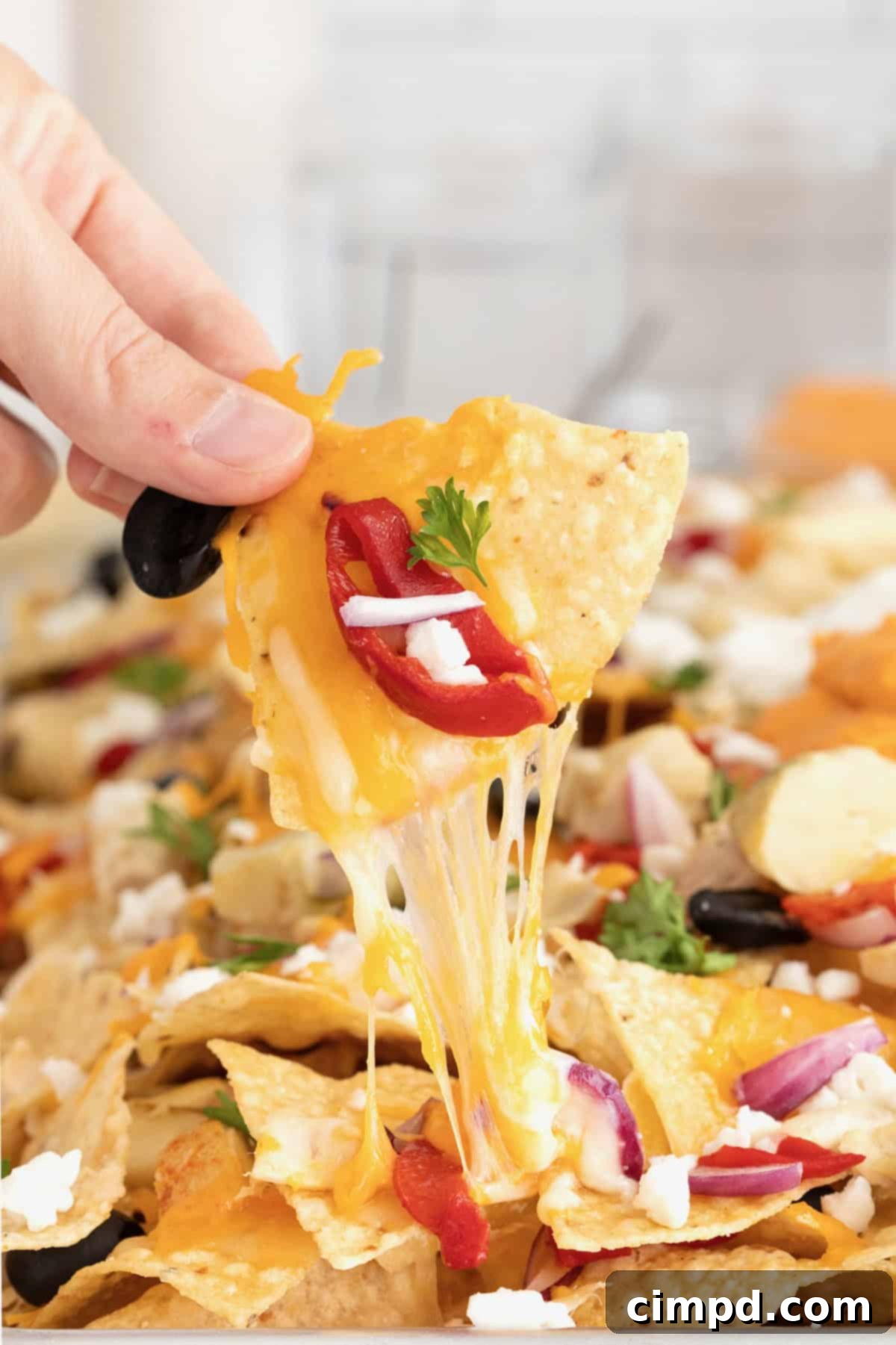 A hand reaching for a piece of Mediterranean nacho, showing the melted cheese and toppings.