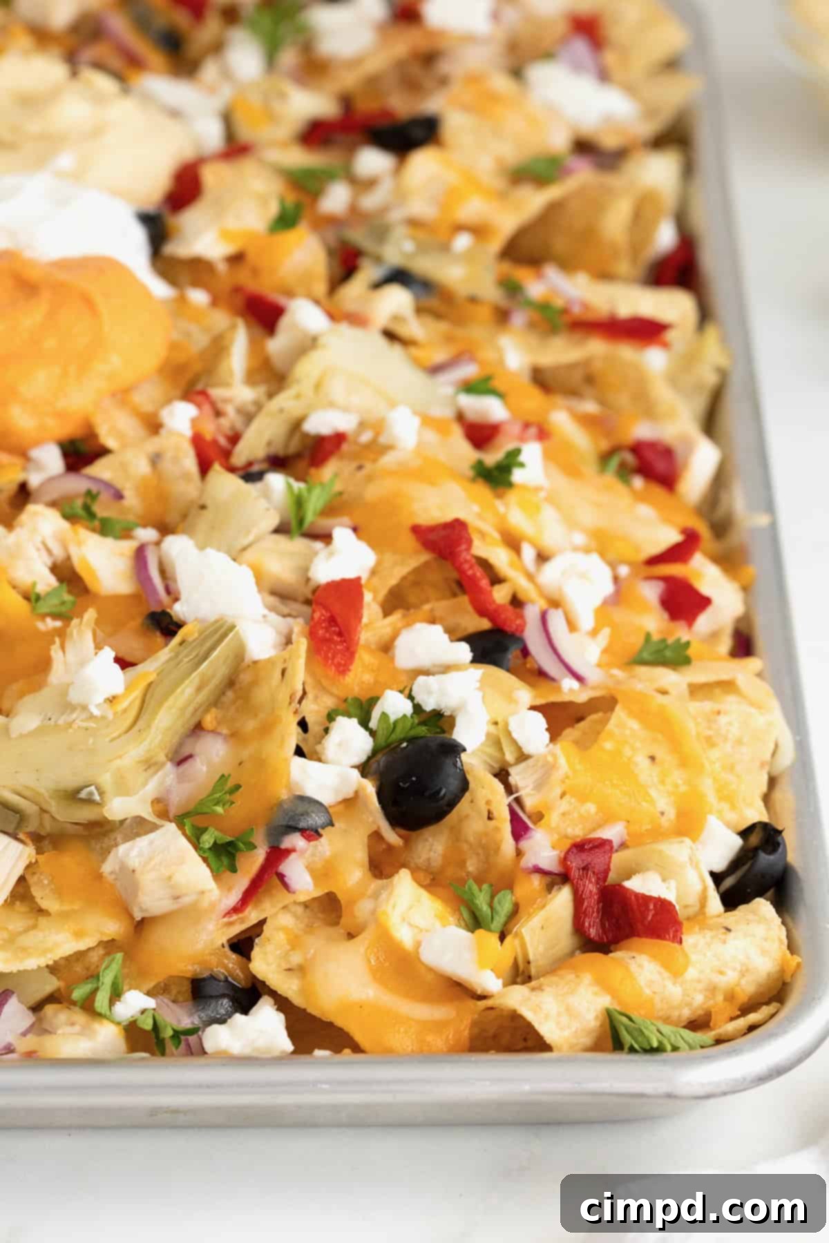 A sheet pan full of pita chip nachos, loaded with toppings, on a white marble counter.