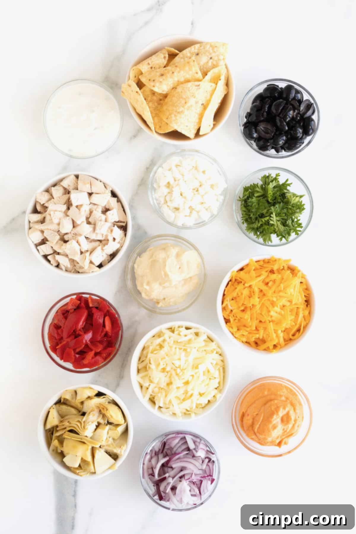 Various ingredients for Mediterranean Nachos, neatly arranged in small glass bowls on a white marble counter.