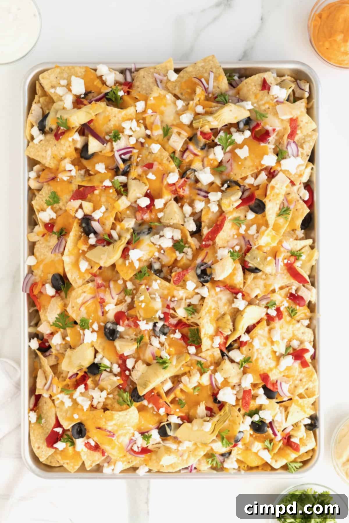 Close-up shot of feta cheese being sprinkled on hot Mediterranean nachos.