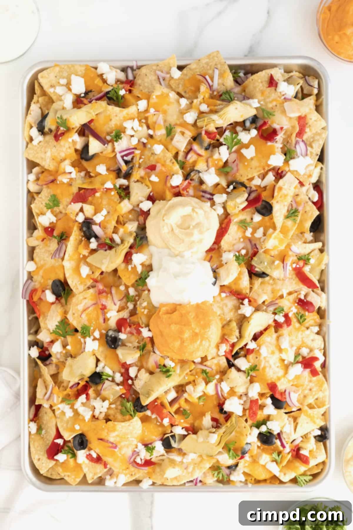 A sheet pan full of pita chip nachos, ready to be served, on a white marble counter.