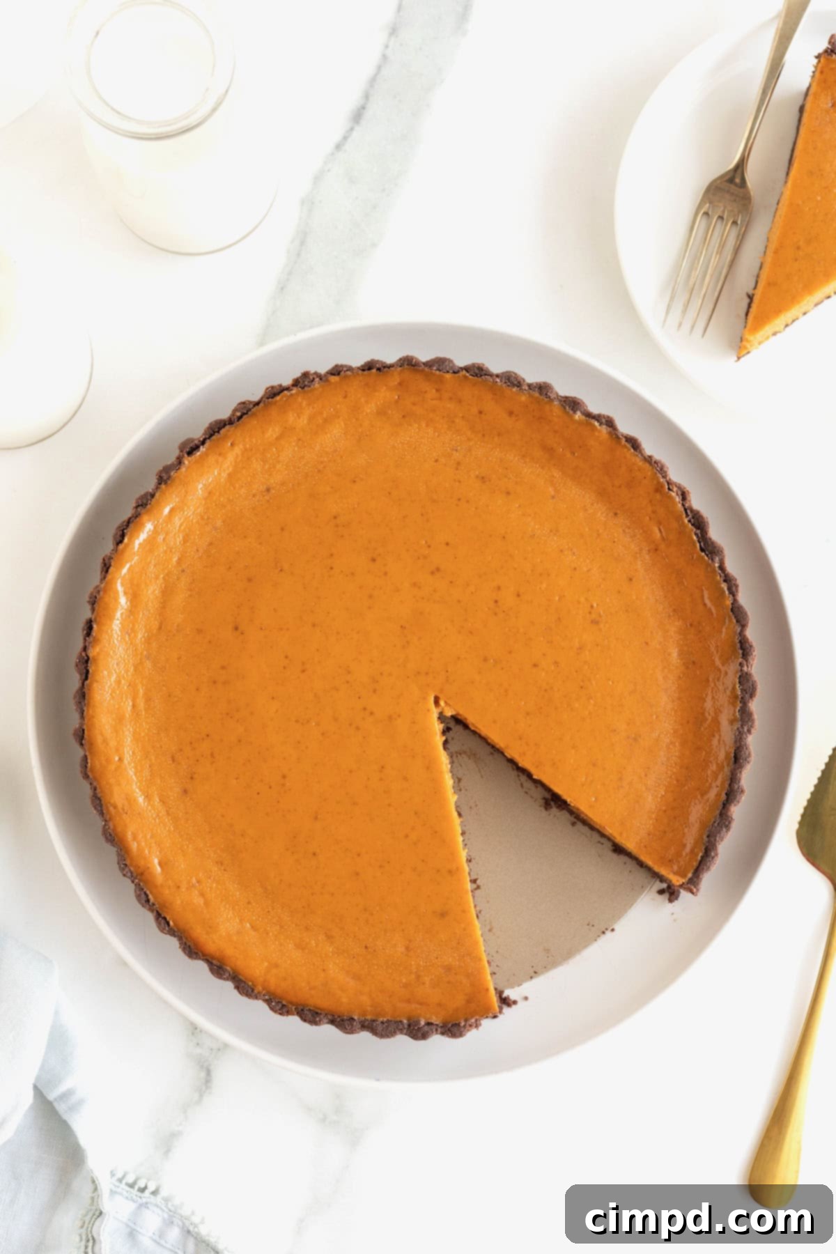 A perfectly baked Dark Chocolate Pumpkin Tart with a rich chocolate crust, resting on an elegant white serving plate. A single slice has been removed, revealing the creamy orange pumpkin filling against the dark chocolate base, inviting you to indulge in its seasonal delight.