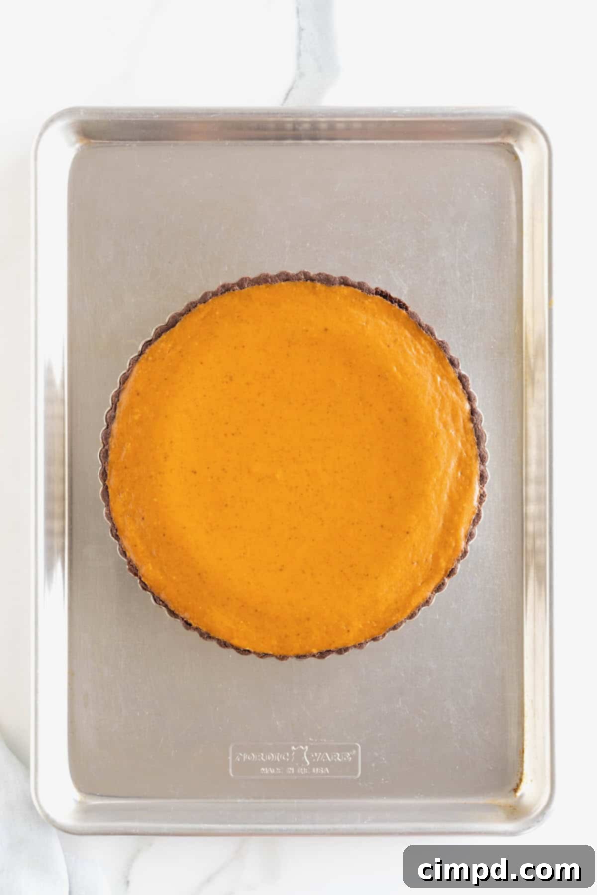 A freshly baked and cooked Dark Chocolate Pumpkin Tart, still warm on an aluminum baking sheet, its filling set and edges golden-brown, ready for cooling.
