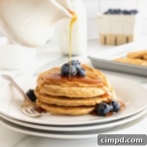 Simple 5-Ingredient Flourless Protein Pancakes 11 A close-up of a stack of fluffy 5-Ingredient Flourless Protein Pancakes, garnished with fresh blueberries and a drizzle of maple syrup, ready to be served.