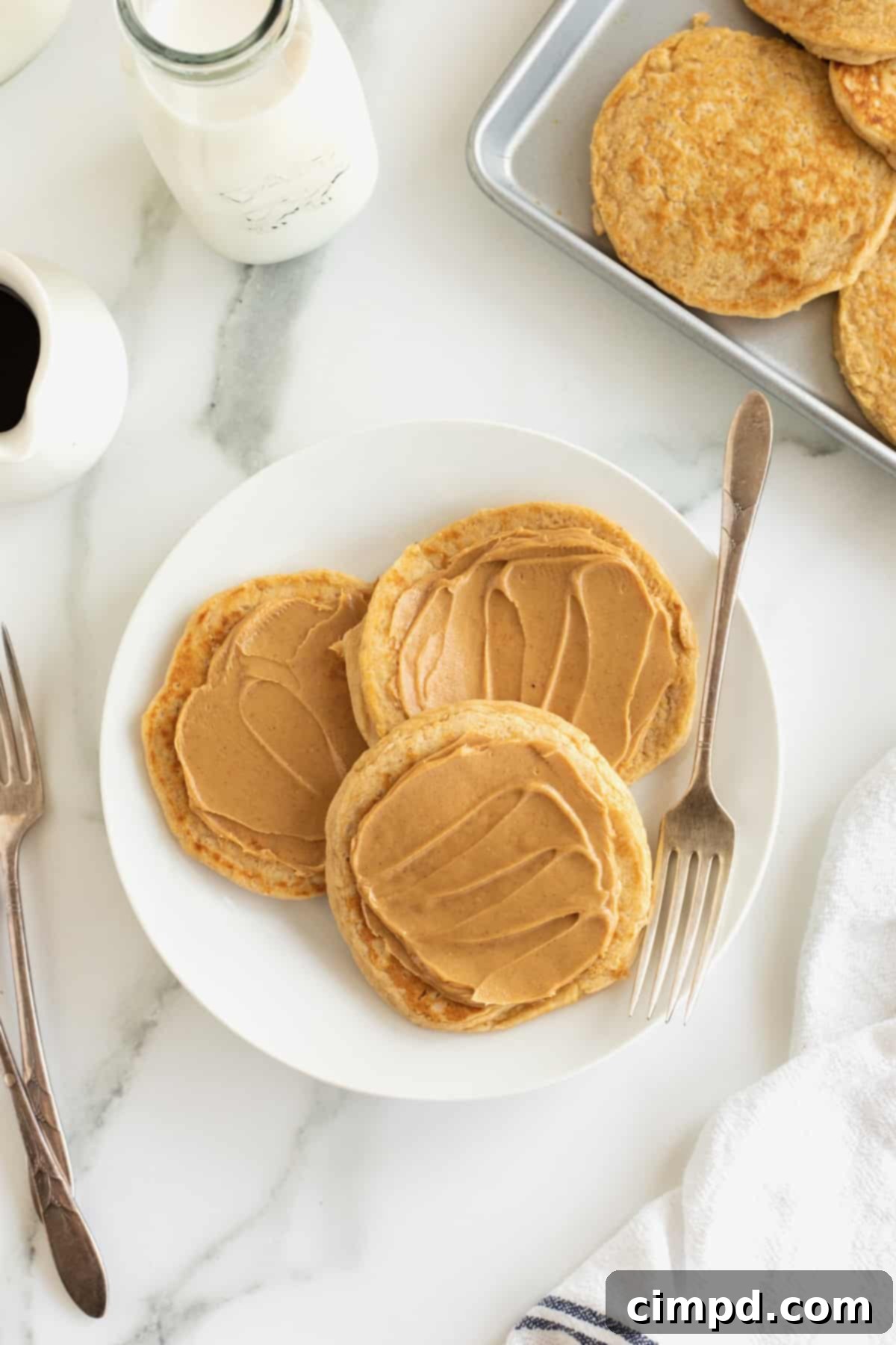 Simple 5-Ingredient Flourless Protein Pancakes 4 Three perfectly cooked flourless protein pancakes, generously topped with melted peanut butter, arranged on a crisp white plate alongside a fork, inviting a delicious breakfast.