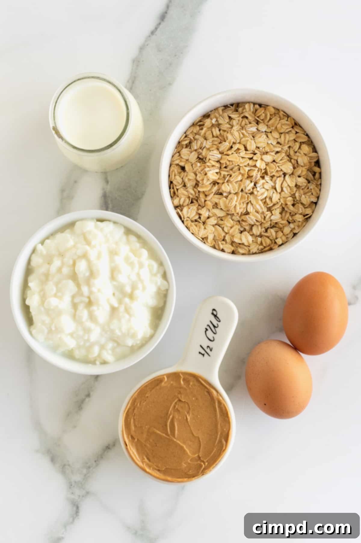 Simple 5-Ingredient Flourless Protein Pancakes 7 A collection of five key ingredients for making flourless protein pancakes: rolled oats, cottage cheese, peanut butter, a glass of milk, and two brown eggs, all neatly arranged on a kitchen counter.