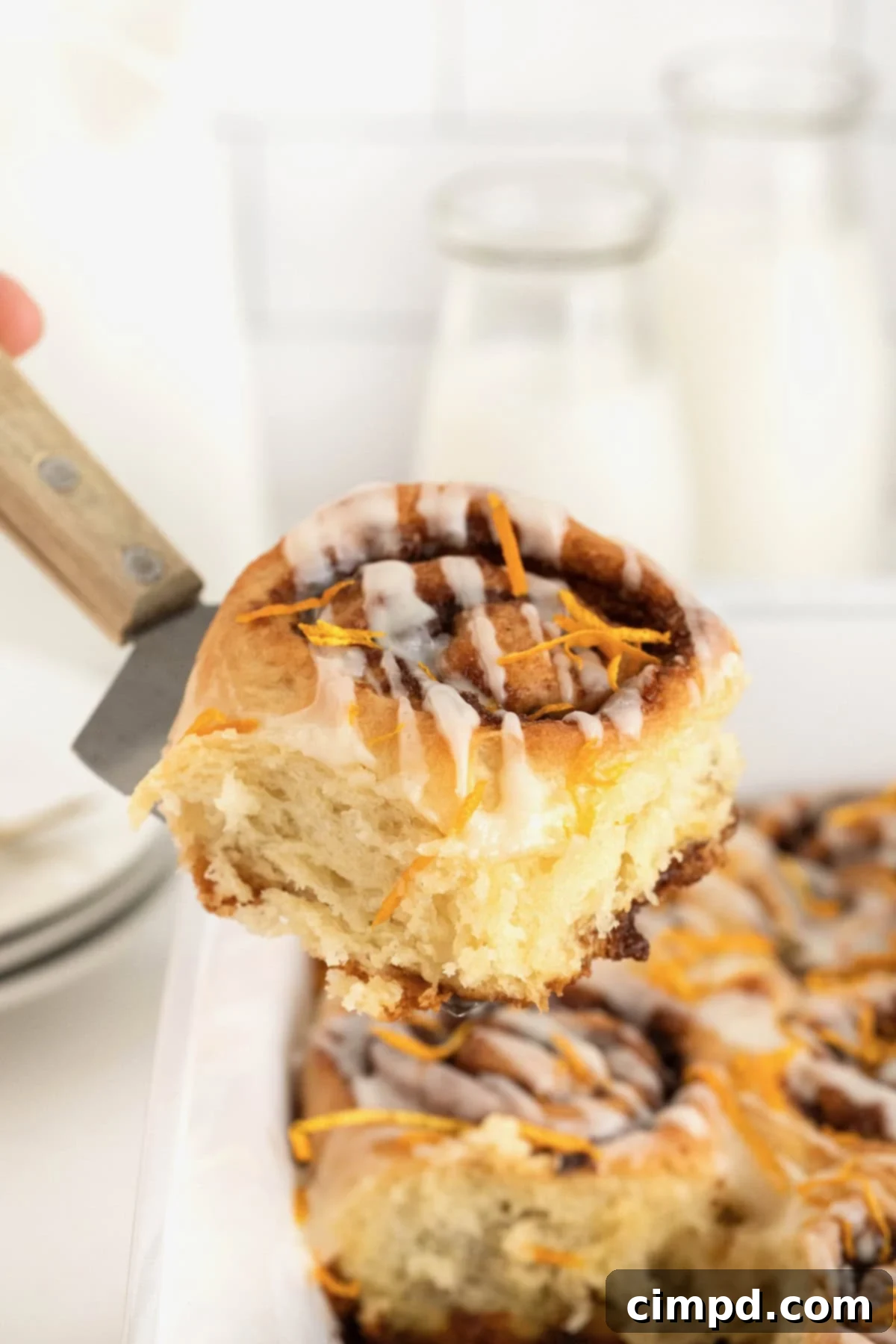 A spatula lifting a chocolate orange cinnamon roll out of a white baking dish, showcasing its gooey center and warm, inviting color.