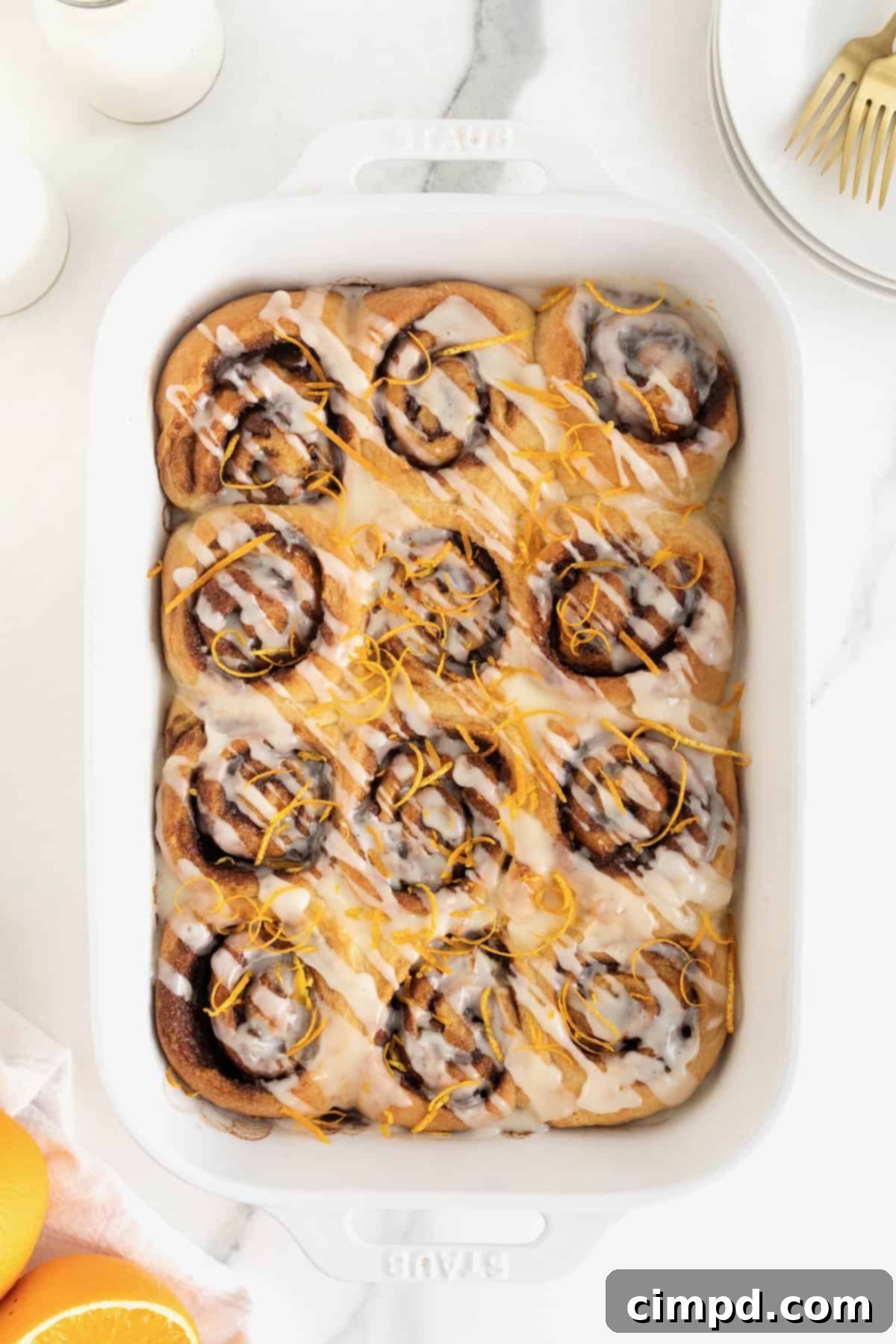A beautifully arranged white baking dish showcasing a batch of freshly baked cinnamon rolls, elegantly topped with vibrant orange zest.