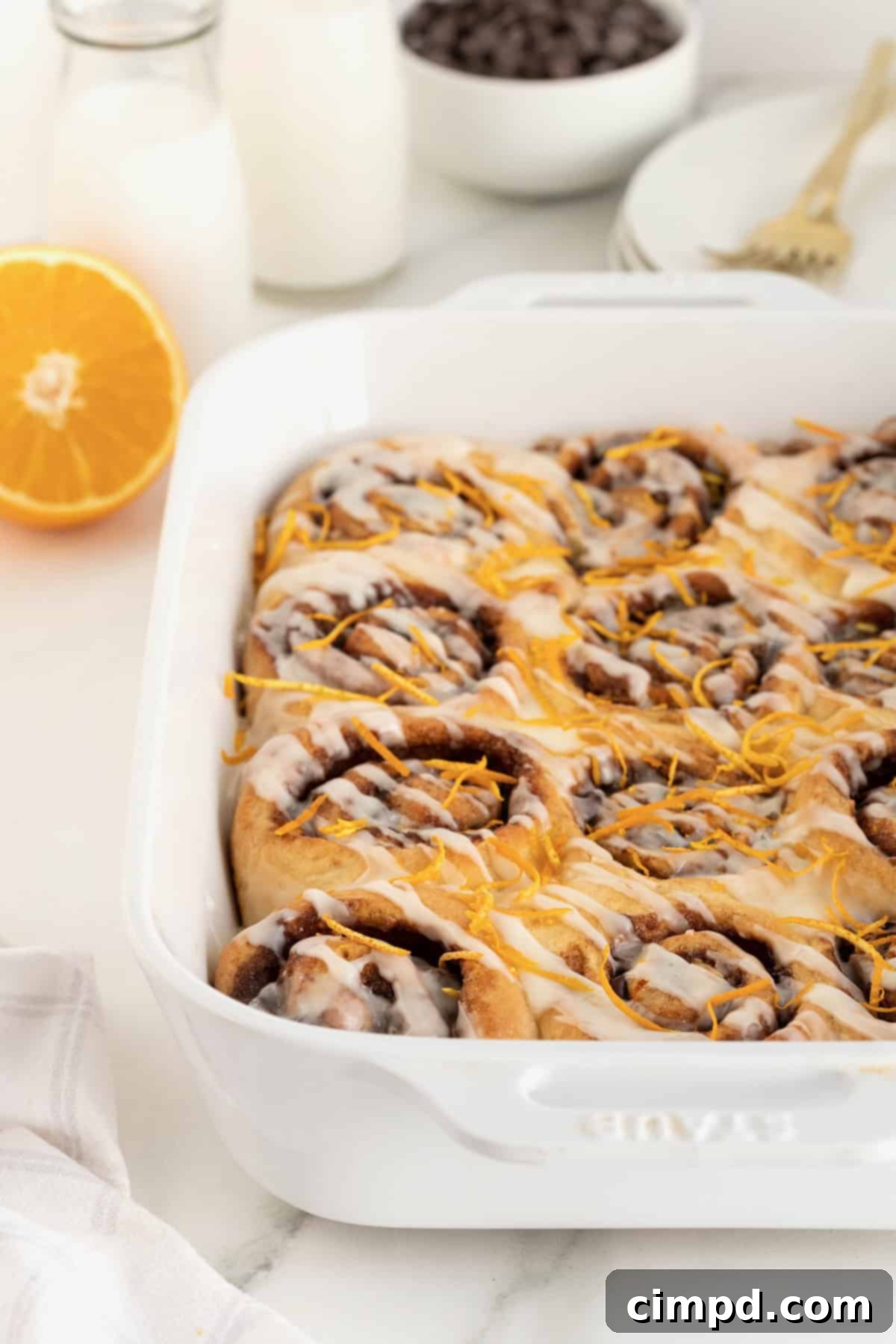 A white baking dish filled with a fresh batch of cinnamon rolls, generously adorned with orange zest, ready for serving or storage.