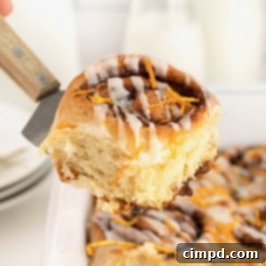 A spatula lifting a chocolate orange cinnamon roll out of a white baking dish.
