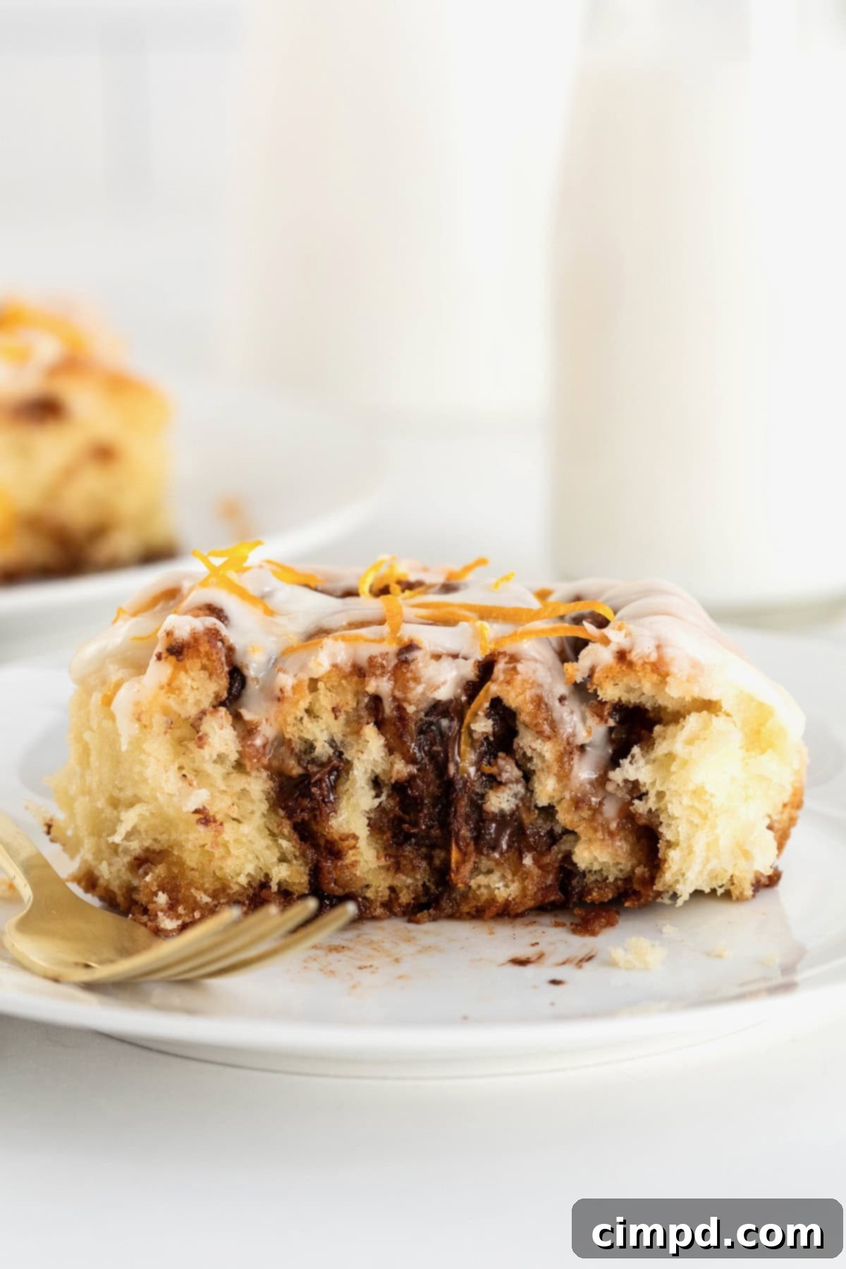 A perfectly cut chocolate orange cinnamon roll, split in half on a small white plate, revealing its intricate layers of dough, chocolate, and cinnamon.