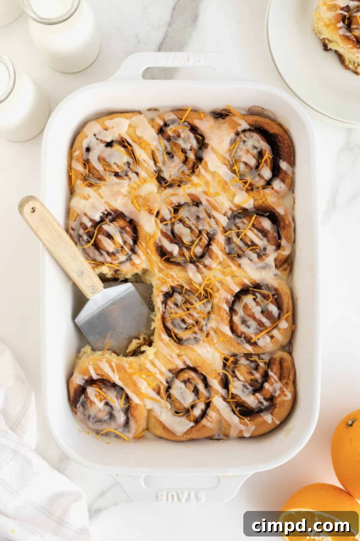 A pristine white baking dish filled with freshly baked cinnamon rolls, adorned with delicate orange zest, ready to be served.