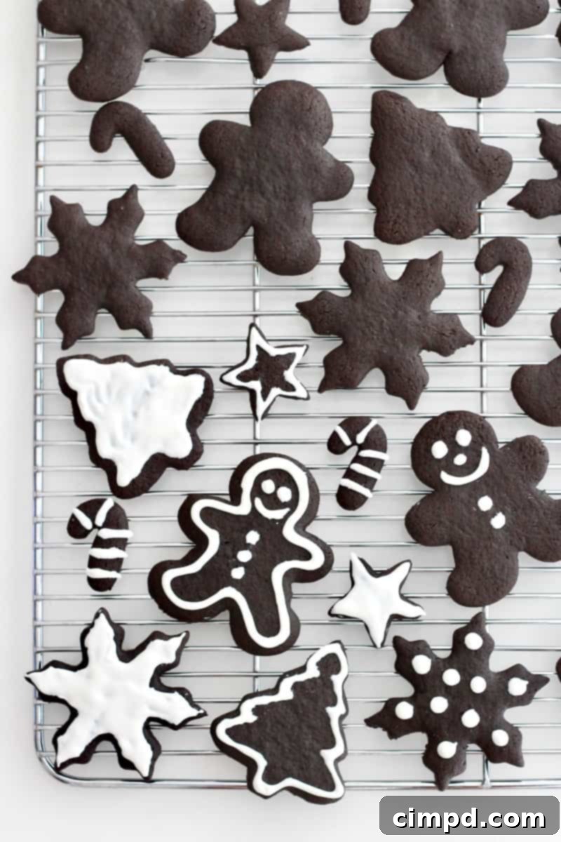 A metal cooling rack with Christmas shaped chocolate cookies of various sizes. Some of the cookies have white icing on them.
