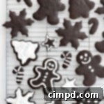 A metal cooling rack with Christmas shaped chocolate cookies of various sizes. Some of the cookies have white icing on them.