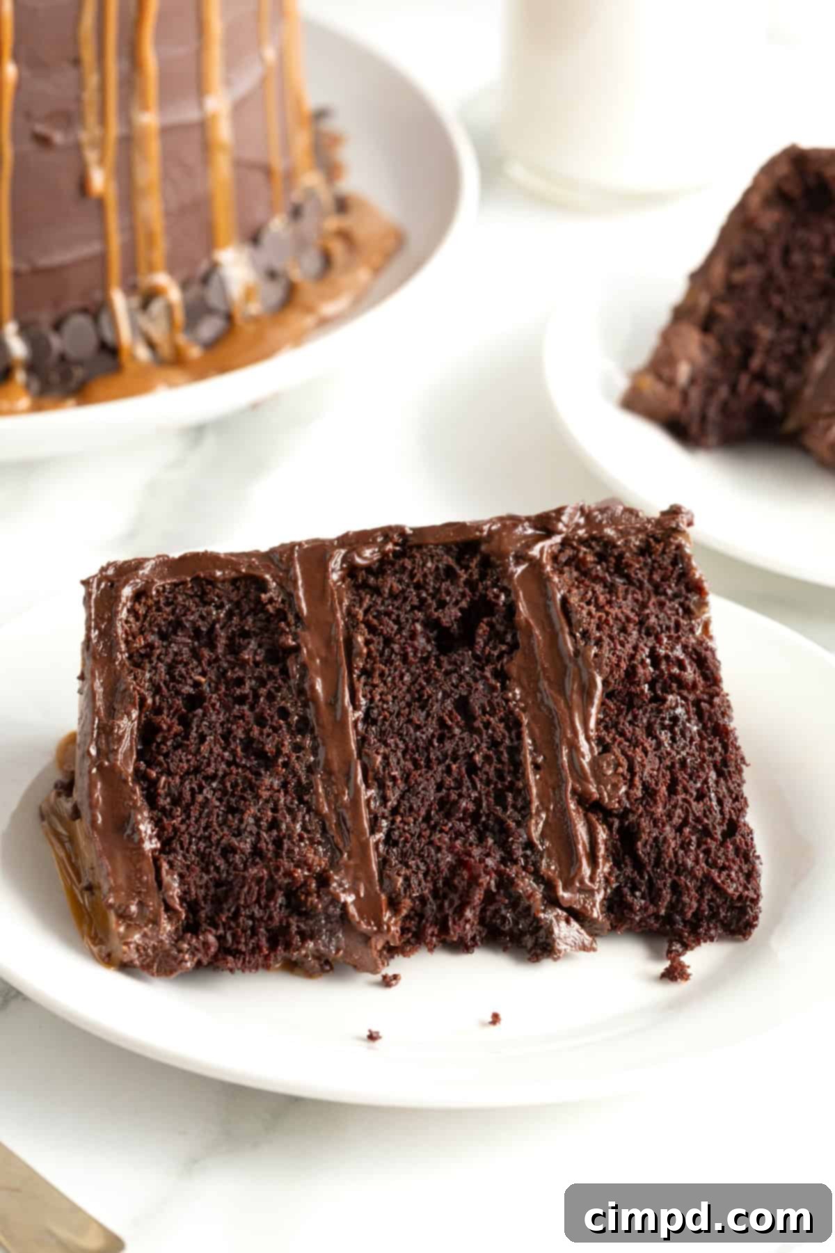 A perfectly portioned slice of chocolate fudge caramel 3 layer cake on its side on a small white dessert plate, revealing its moist layers and generous fillings.