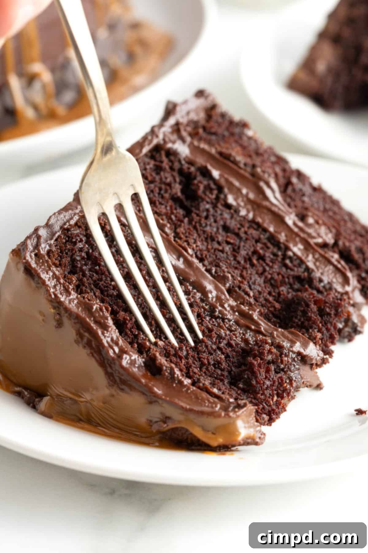 A delectable slice of chocolate fudge caramel 3 layer cake, leaning on its side on a small white dessert plate, showcasing its rich texture and layers.