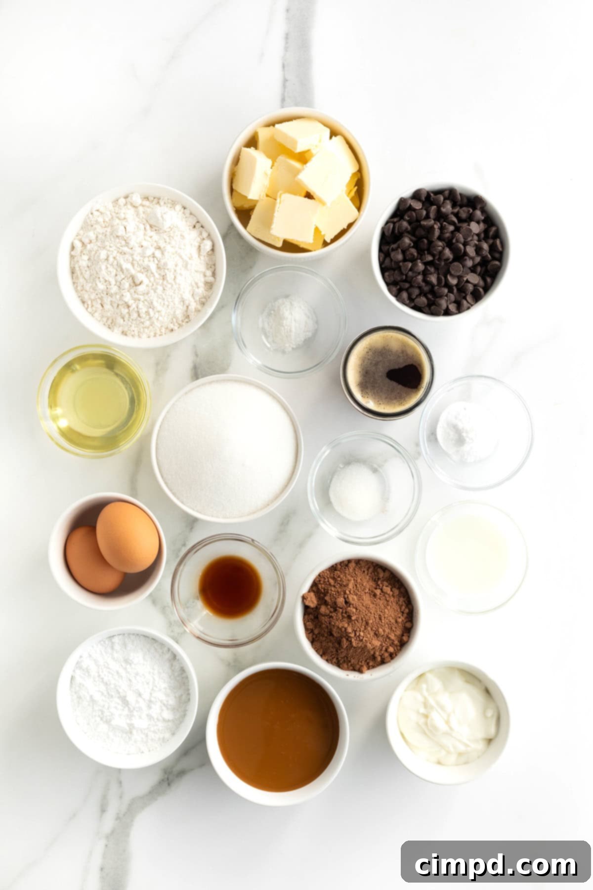 A collection of ingredients neatly arranged in small white bowls on a pristine white marble counter, ready to be used for making a fudge caramel stout cake.