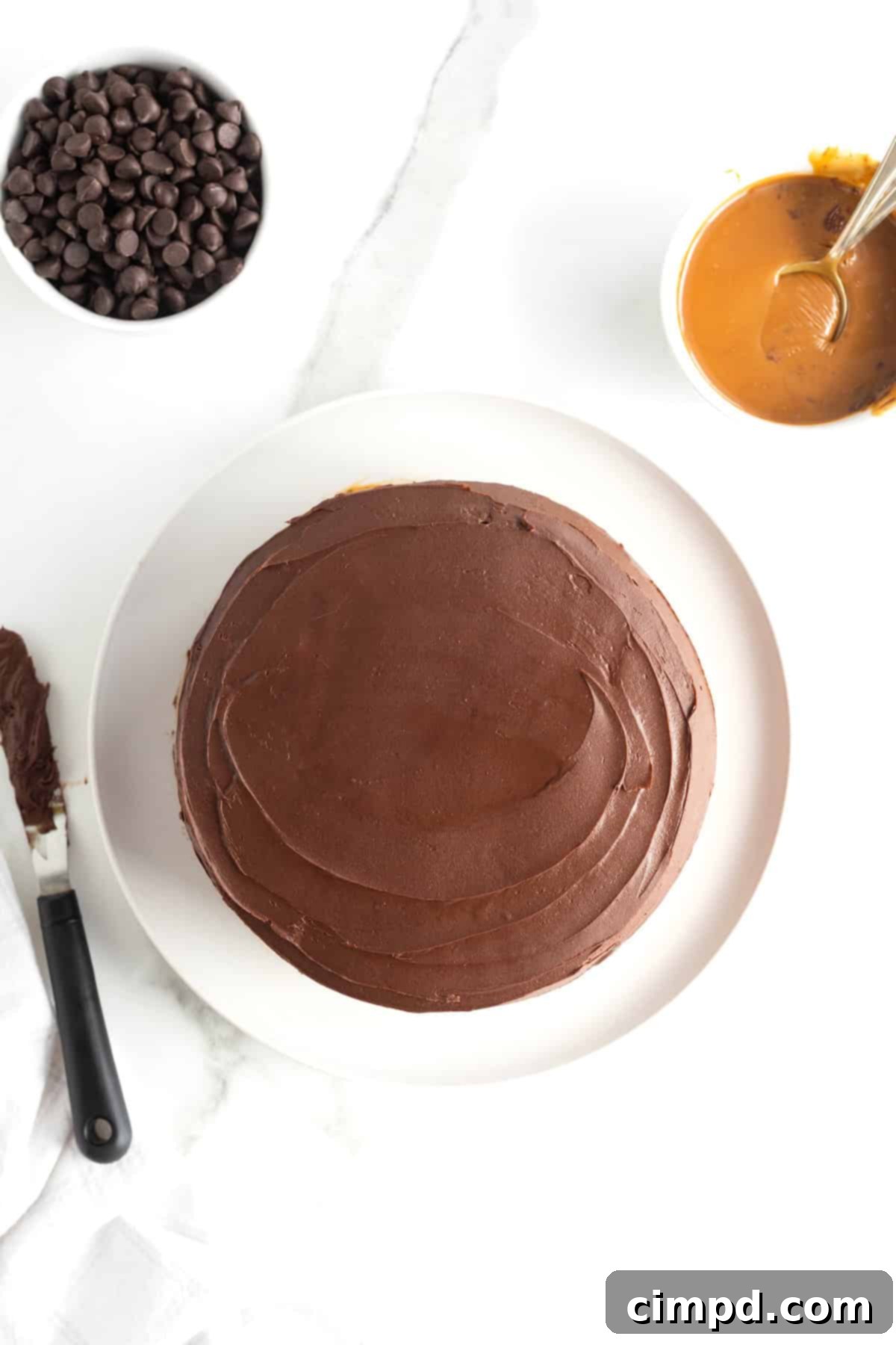 A beautiful top-down view of a fully iced chocolate cake resting on a white serving plate, perfectly smooth and ready for decoration.