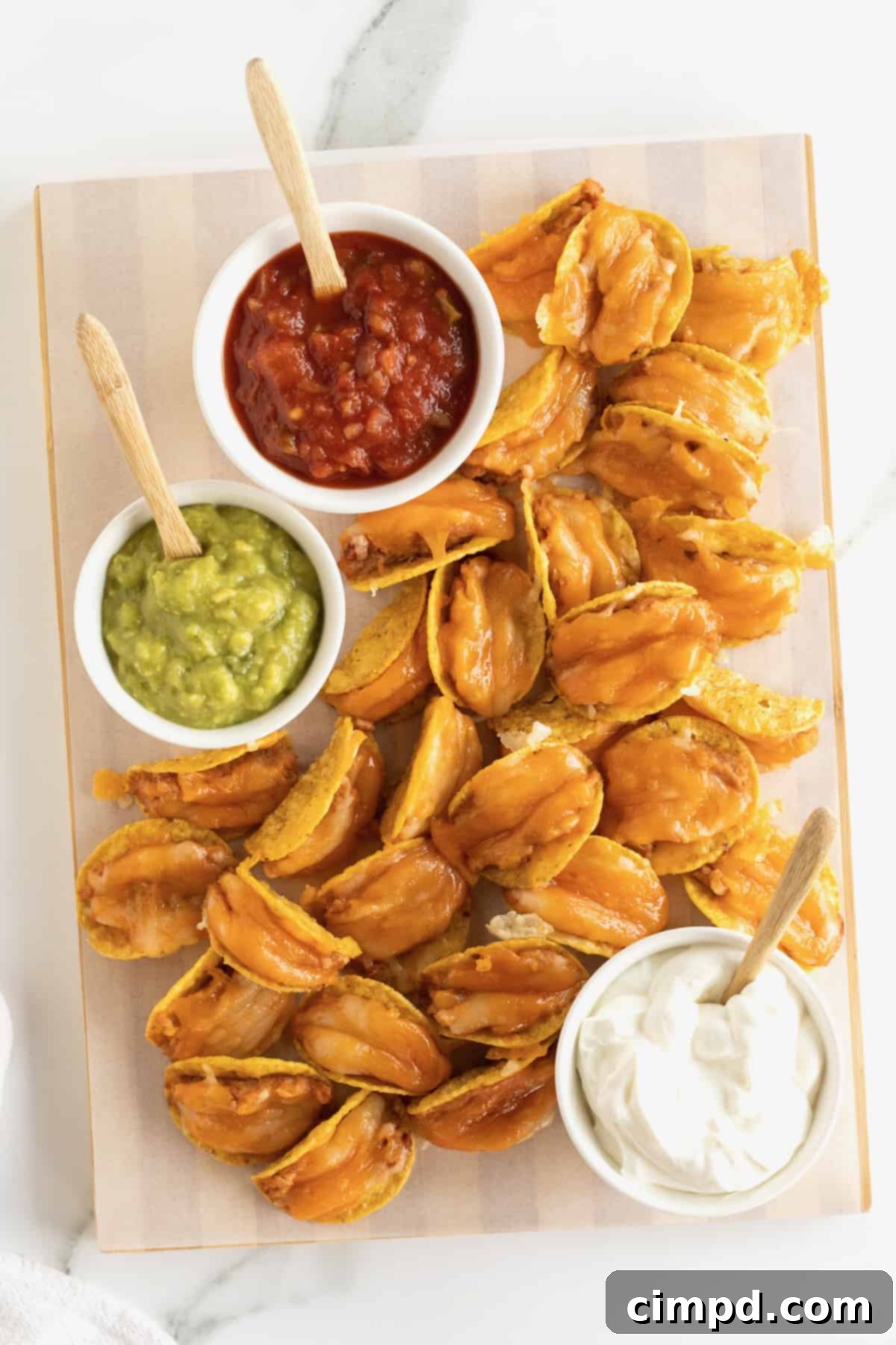 Taco bites made out of tortilla chips, refried beans and cheese served with a bowl of guacamole and a bowl of salsa.