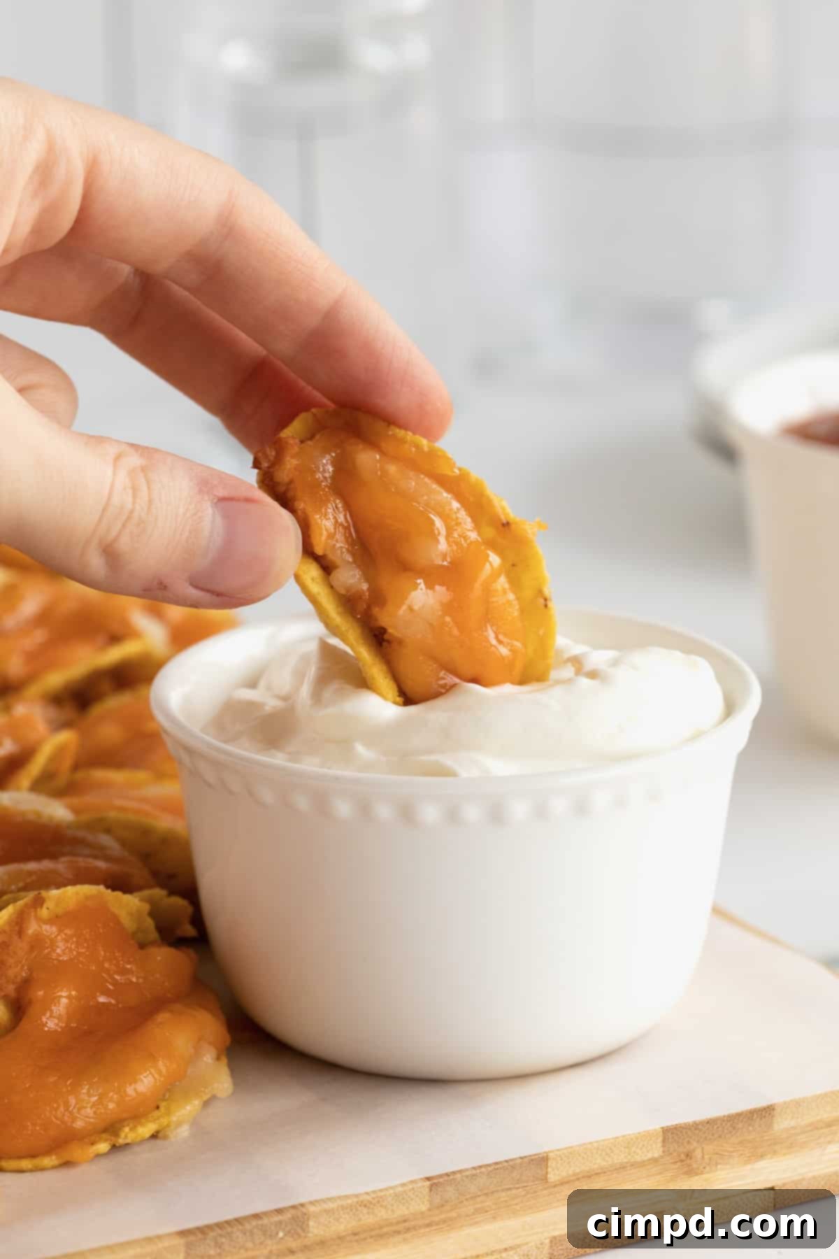 A taco bite made out of tortilla chips, refried beans and cheese dipped in sour cream.
