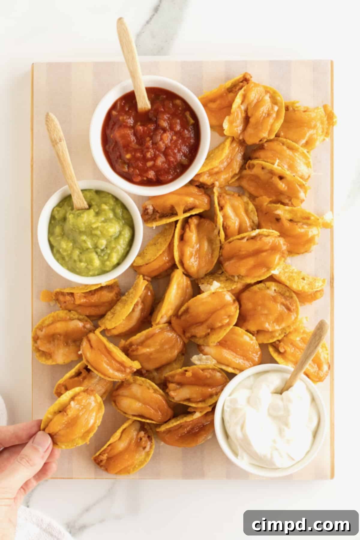 Taco bites made out of tortilla chips, refried beans and cheese served with a bowl of guacamole, sour cream and a bowl of salsa.