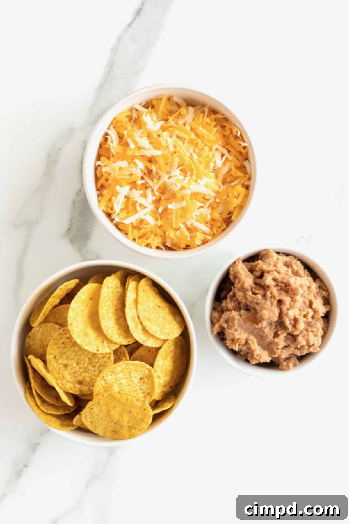 Shredded cheese, round tortilla chips, and refried beans in small bowls.