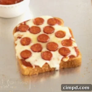 A close-up of a delicious piece of pizza toast on a baking sheet, with a small bowl of marinara sauce in the background.