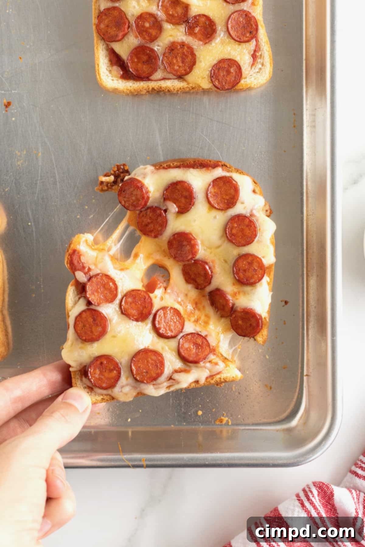 A piece of pizza toast, neatly cut into two triangles, presented on an aluminum baking sheet.