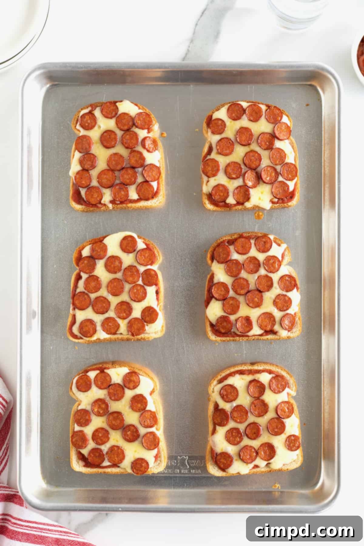 Six golden-brown pieces of pizza toast, cheese bubbling, arranged on an aluminum rimmed baking sheet, fresh out of the oven.