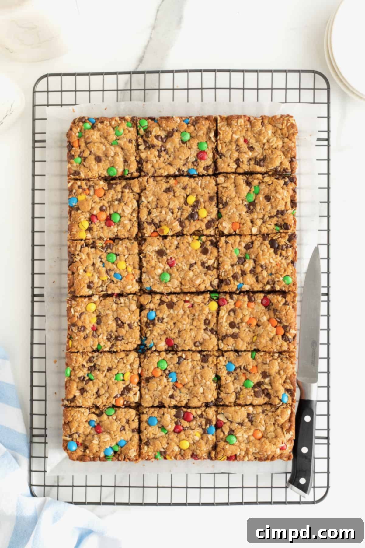 Flourless Monster Cookie Bars cooling on a parchment-lined metal rack, with a chef's knife resting beside them, ready for slicing.