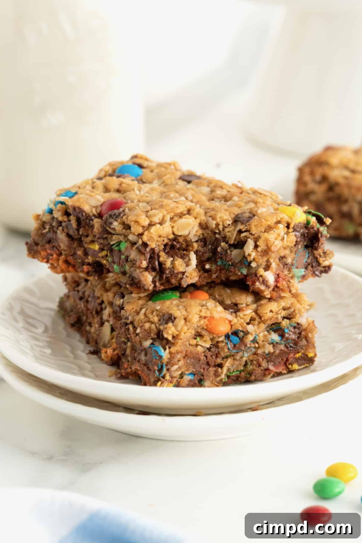 A small white plate elegantly holding two stacked monster cookie bars, inviting a moment of sweet indulgence.