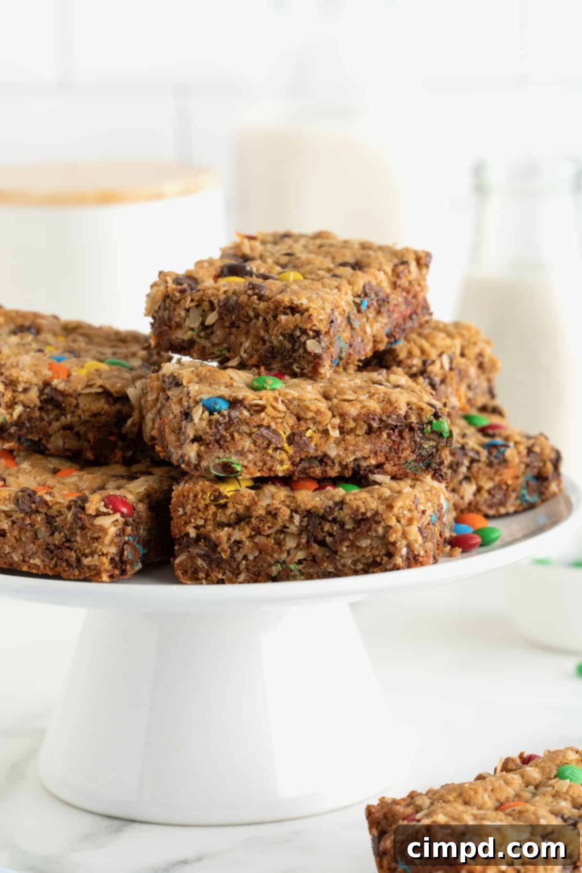 A elegant white cake stand generously piled with an assortment of colourful monster cookie bars, inviting guests to indulge.