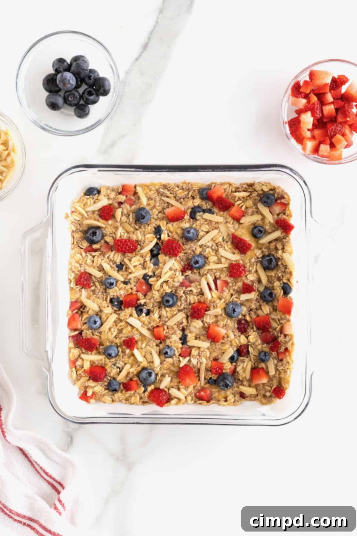 Overnight Oats Bars topped with almond slivers, chopped strawberries and whole blueberries pressed into an 8x8 glass baking dish lined with parchment.