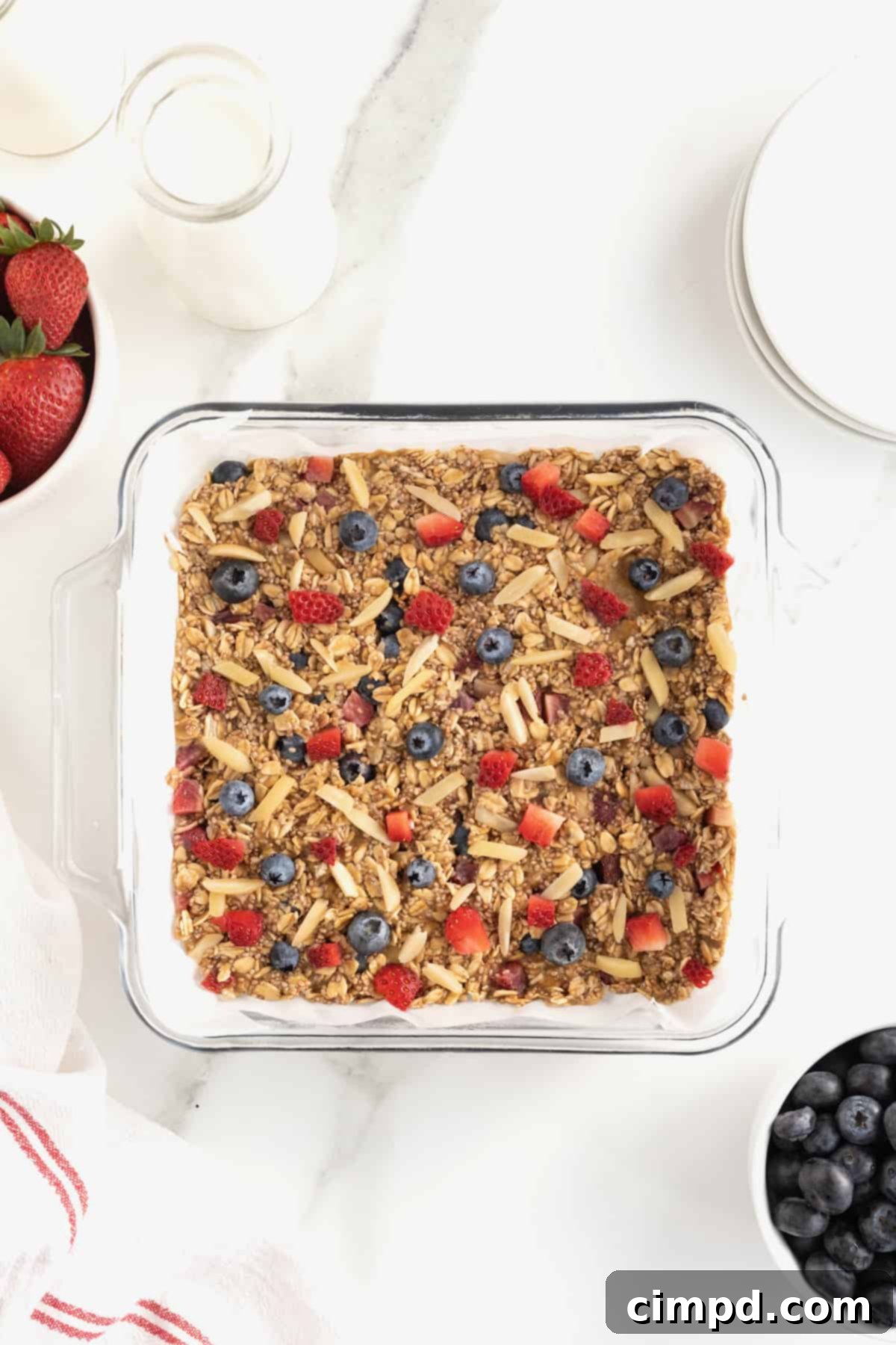 Overnight Oats Bars topped with almond slivers, chopped strawberries and whole blueberries pressed into an 8x8 glass baking dish lined with parchment.
