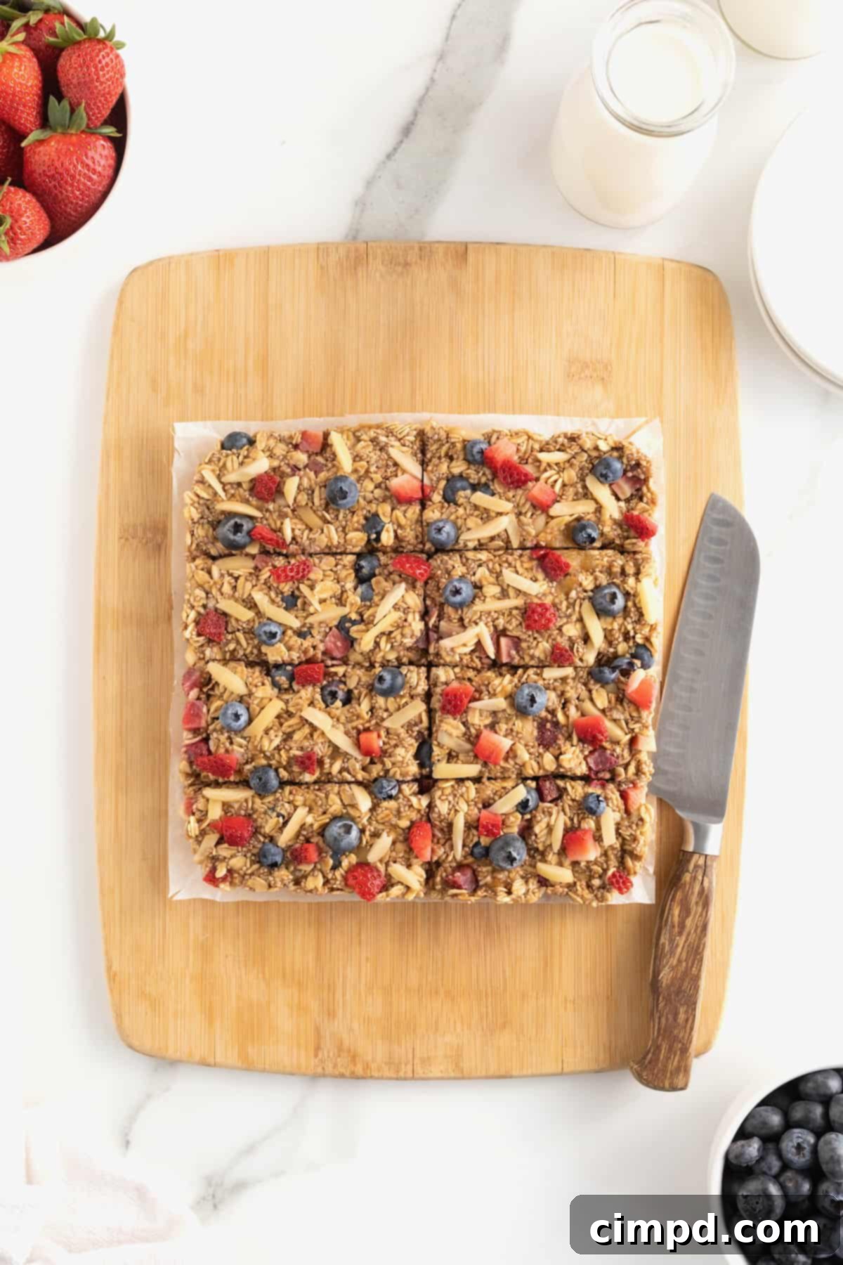 A square of overnight oats bars cut into 8 individual bars on a square of parchment on a rectangular wood cutting board. A knife lays to the right of the bars on the cutting board.