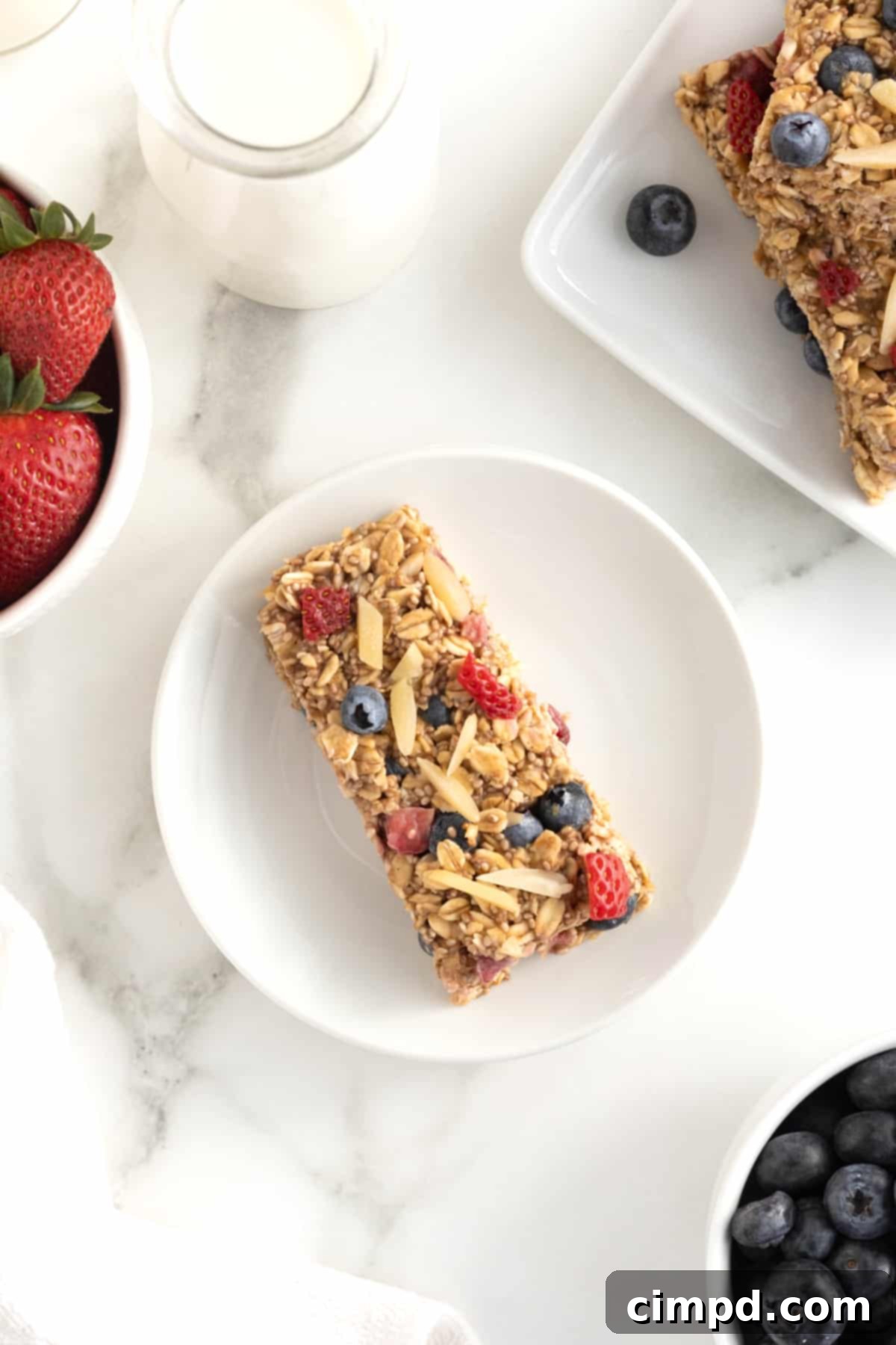 An overnight oats bar topped with strawberry pieces, whole blueberries and almond slivers on a small white plate.