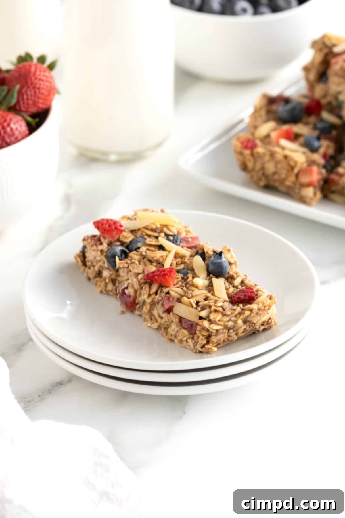 An overnight oats bar topped with strawberry pieces, whole blueberries and almond slivers on a small white plate.