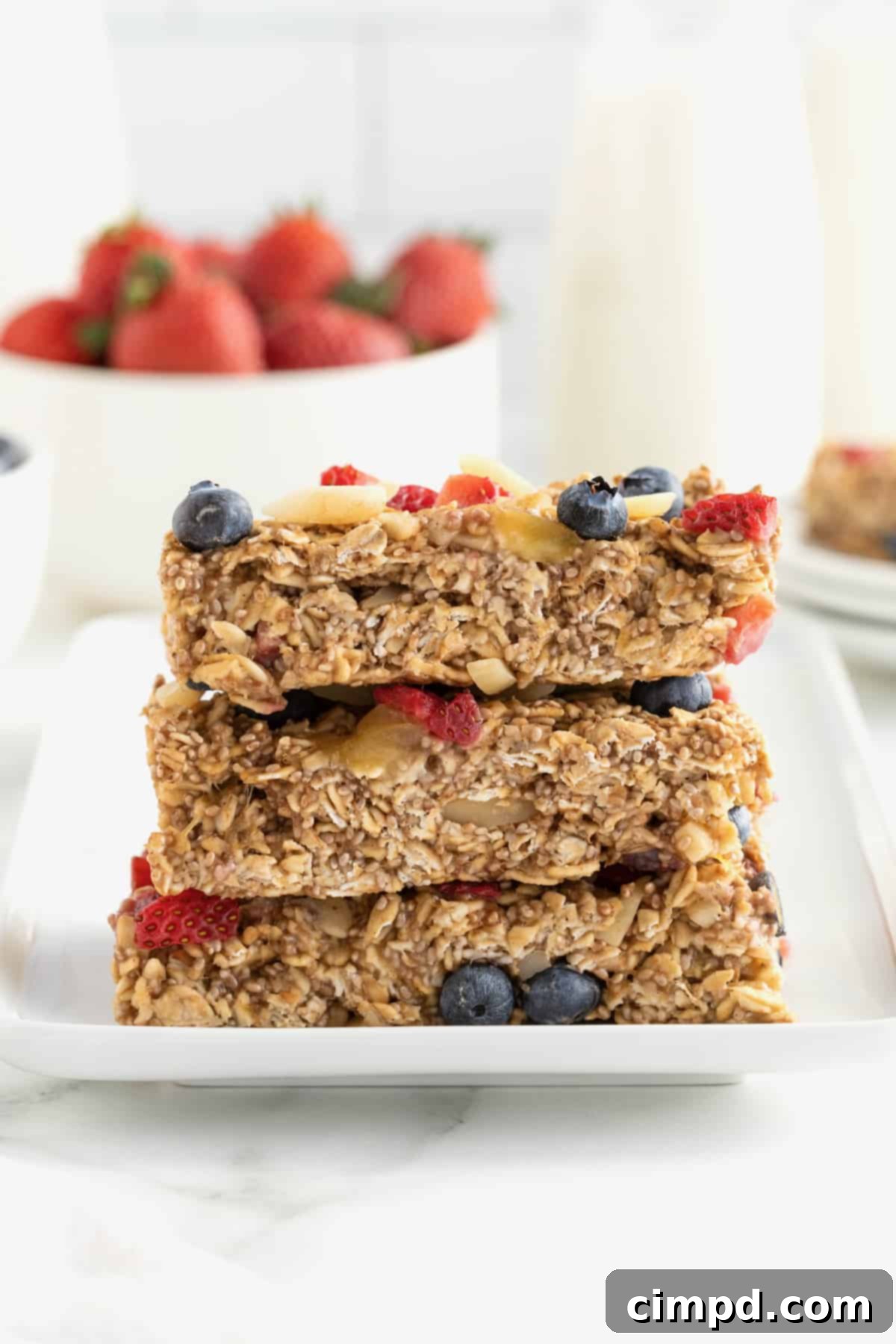 Three overnight oats bars topped with strawberry pieces, whole blueberries and almond slivers on a rectangular white serving plate.