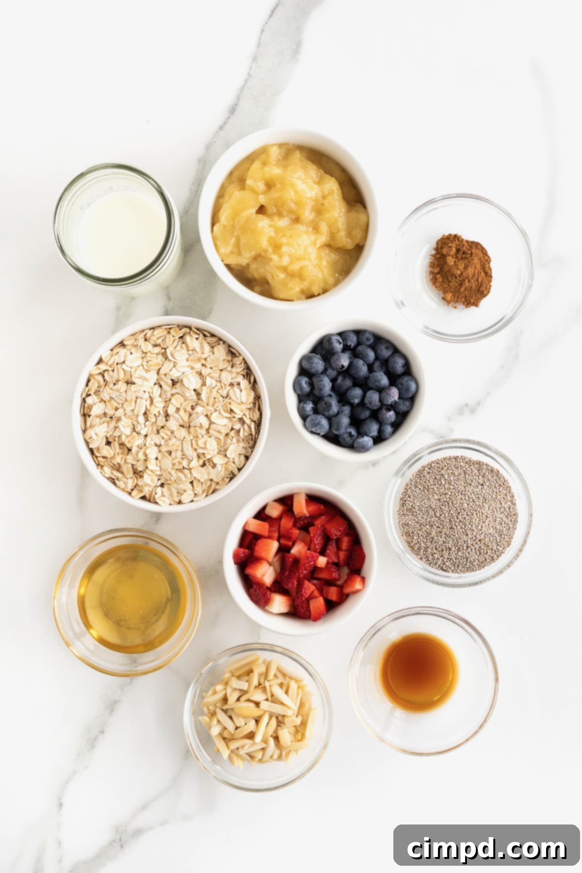 Ingredients to make overnight oats bars in small glass containers on a white marble counter.