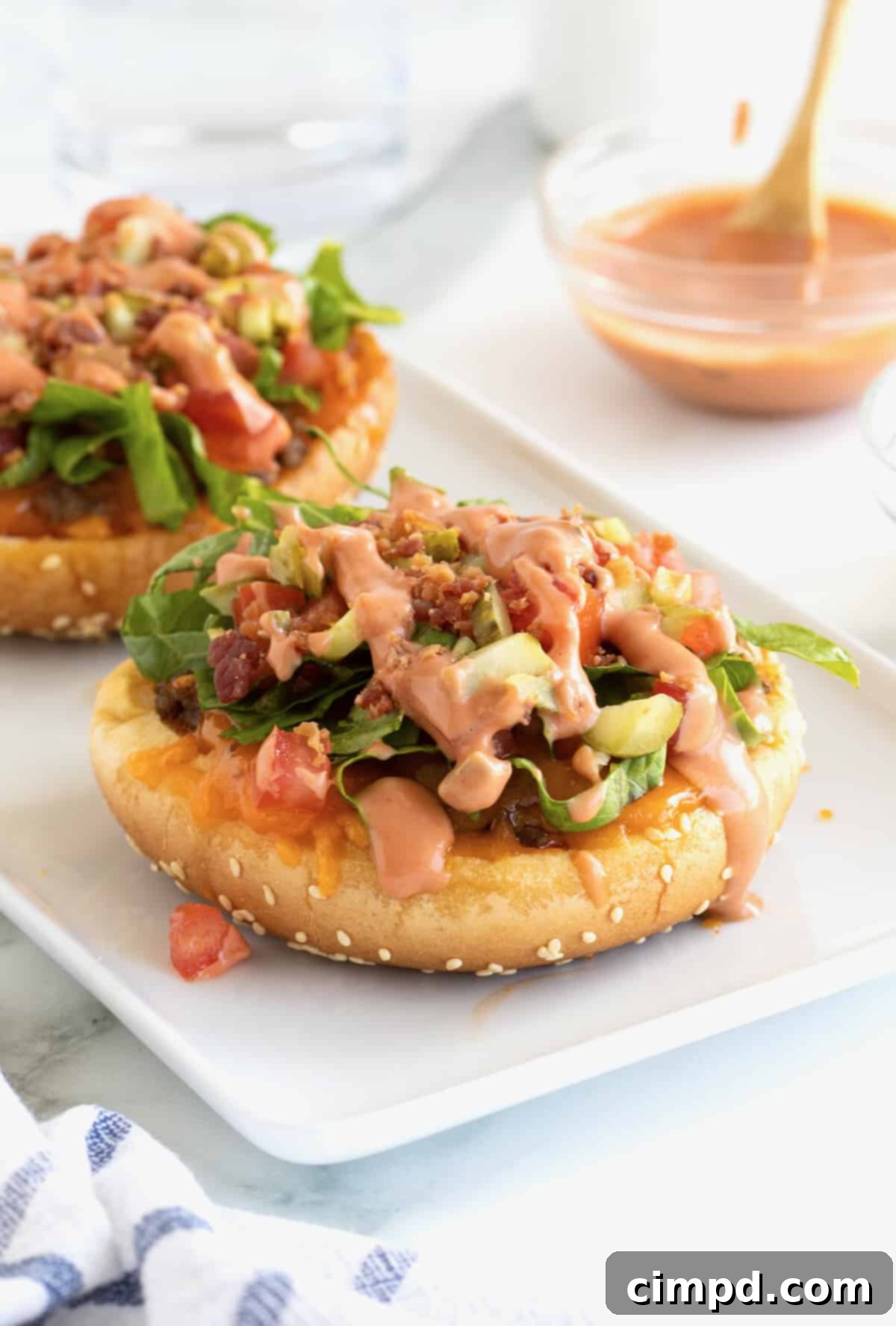 Hamburger buns topped with ground beef and other toppings on a white serving tray, showcasing the delicious Cheeseburger Bun Pizzas.