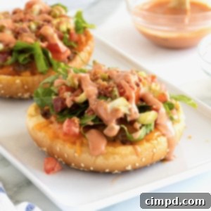 Hamburger buns topped with ground beef and other toppings on a white serving tray.
