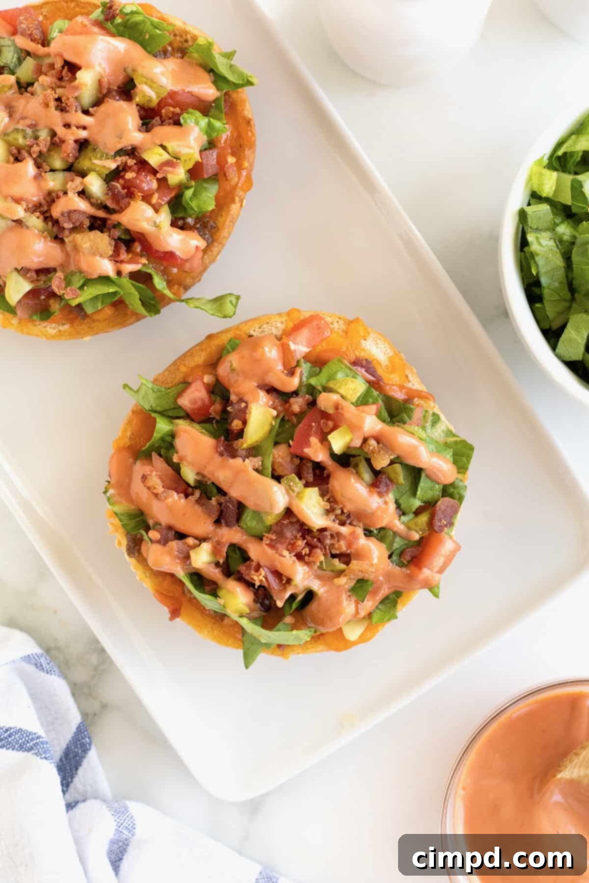 Another view of hamburger buns topped with ground beef, cheese, and other burger-inspired toppings on a white serving tray.
