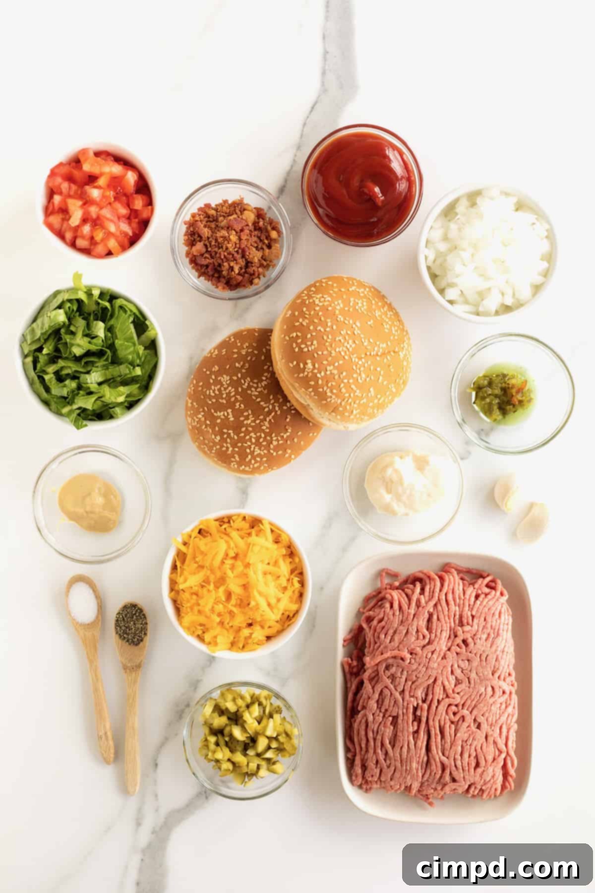 All the fresh ingredients for cheeseburger pizzas laid out on a white countertop, including buns, beef, cheese, and vegetables.